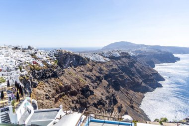 Santorini, Yunanistan - 15 Ekim 2024: Santorini 'deki kayalık köy, beyazlatılmış evler ve berrak mavi gökyüzü altında çarpıcı bir okyanus manzarası