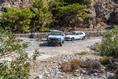 Girit, Yunanistan - 18 Ekim 2024: Agia Roumeli 'deki Samaria Vadisi' nin sonuna yakın park etmiş araçlar, dağılmış ağaçlar ve köye giden kayalık yollarla engebeli araziler sergiliyor.