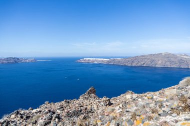 Santorini 'deki kayalık arazi, panoramik Ege denizi ve adanın kayalıklarına yapışan Oia' nın uzak beyaz boyalı binaları..
