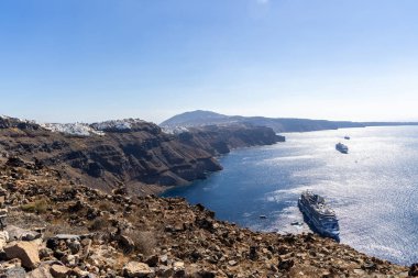 Santorini, Yunanistan - 15 Ekim 2024: Santorini 'nin dramatik uçurumlarının altında Ege Denizi' nde parlak güneş ışığı altında demirli seyahat gemileriyle Oia 'nın panoramik manzarası.