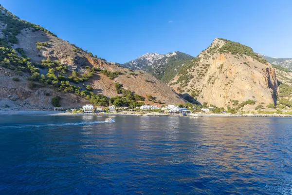 Girit, Yunanistan - 18 Ekim 2024: Samarya Boğazı 'nın sonundaki kayalıkların kenarındaki bir köyün manzarası, teknelerin körfezin sakin sularına demir attığı yer.
