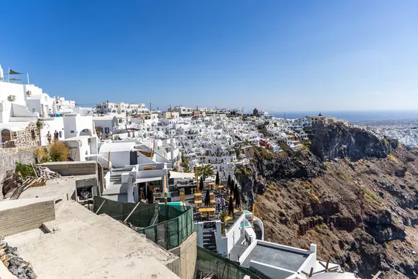 Santorini, Yunanistan - 15 Ekim 2024: Santorini 'de manzaralı okyanus manzaralı ve mavi gökyüzü olan kayalıklardaki beyaz evlerin panoramik manzarası. İkonik Yunan adası cazibesi