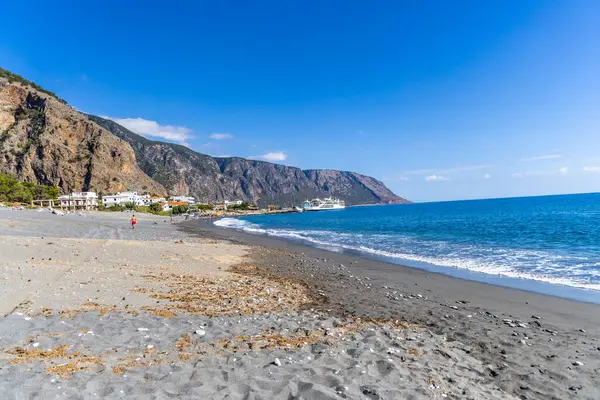 Girit, Yunanistan - 18 Ekim 2024: Libya Denizi 'ndeki sakin Agia Roumeli köyü, sahil turkuaz suları ve kıyıda bekleyen feribotlarla Samarya Boğazı çıkışında.