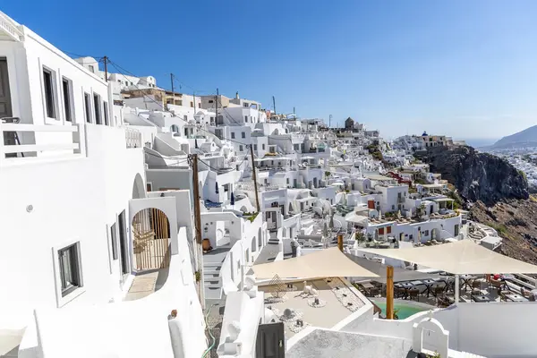 Santorini, Yunanistan - 15 Ekim 2024: Santorini 'de kayalıkların kenarındaki beyaz evler ve mavi kubbeli kiliseler manzaralı. İkonik Yunan ada mimarisi ve canlı atmosferi