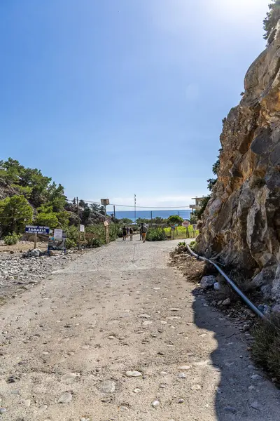 Girit, Yunanistan - 18 Ekim 2024: Samiriye Vadisi 'nin sonu Agia Roumeli kıyı köyüne giden yol, kayalık uçurumların ötesindeki deniz manzarasını ve yolu gösteren işaretler..