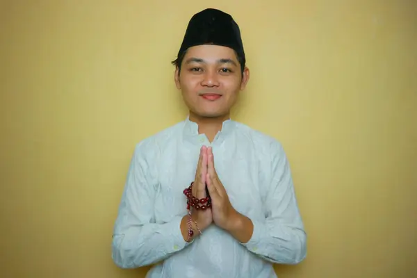 an Indonesian Muslim man of Asian descent wearing Muslim clothes and a black peci, celebrating Eid al-Adha, Eid al-Fitr. Isolated on a yellow background and with very diverse expressions