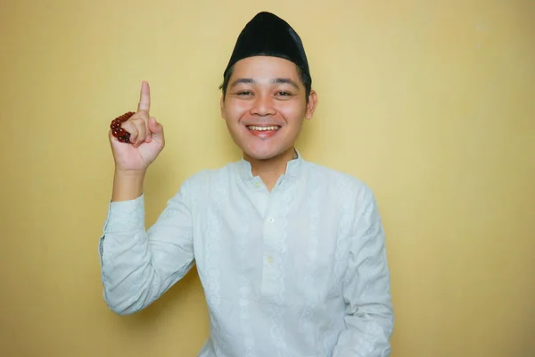 an Indonesian Muslim man of Asian descent wearing Muslim clothes and a black peci, celebrating Eid al-Adha, Eid al-Fitr. Isolated on a yellow background and with very diverse expressions