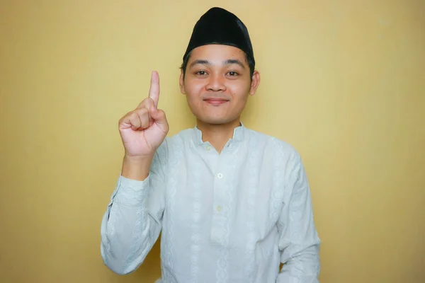 一名身穿穆斯林服装 头戴黑色胸针的亚裔印度尼西亚穆斯林男子 庆祝开斋节开斋节 隔离在黄色背景上 有各种各样的表达方式 — 图库照片