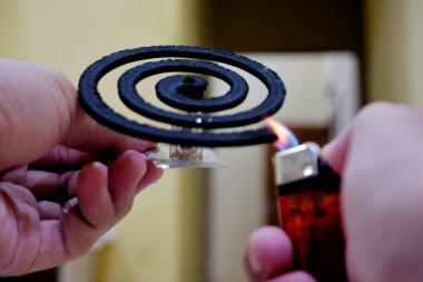 Birinin elinde siyah, dumansız bir sivrisinek kovucu ve kırmızı bir çakmak var.