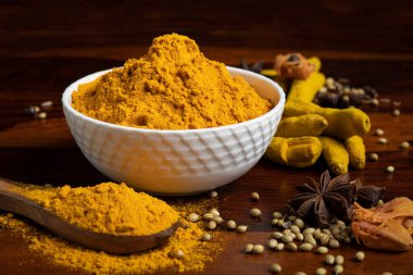 Bir kase sarı zerdeçal tozu ahşap kaşık içinde zerdeçal tozu, yıldız anason, hindistan cevizi, kimyon, kişniş tohumu, kuru zerdeçal kökü ve ahşap karabiber içeren kuru baharatlar.