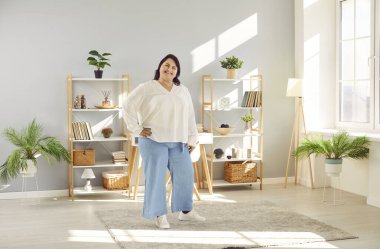 Şişman, iri yarı esmer bir kadının oturma odasında oturmuş gülümseyen uzun bir portresi. Şişman, neşeli bir kız kameraya olumlu bakıyor. Vücut pozitif konsept.