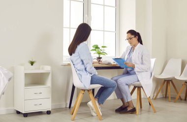 Kadın bir jinekolog, genç hamile bir kadının tansiyonunu ölçüyor. Sağlık muayenesi sırasında ve raporunu randevuyla birlikte tutuyor. Sağlık ve hamilelik kavramı.