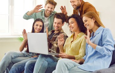 Genç mutlu öğrenci portresi kanepede oturuyor ve bir arkadaşla veya iş arkadaşıyla evdeki bir laptopta görüntülü görüşme yapıyor. İnternet iletişimi, blog yazma kavramı.