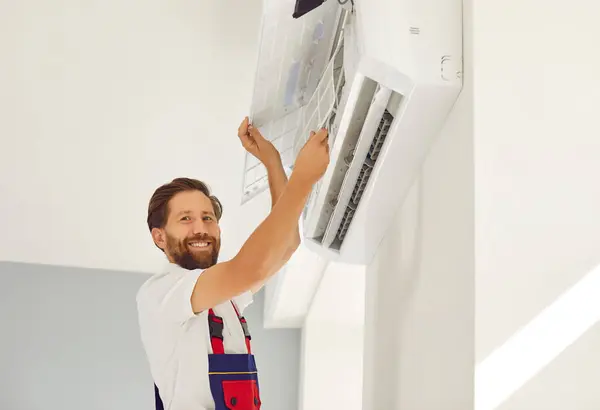 Portrait of smiling male technician in work uniform installing or repairing air conditioner. Technician is installing air conditioning equipment with screwdriver. Concept of technician service.