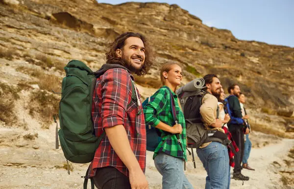 Happy tourist people, outdoor hiking travelling group walking on countryside trail, mountain footpath. Friends enjoy backpack tour, nature recreational activity, natural environment journey, discovery