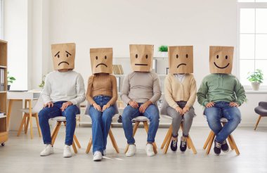 İnsani duygular. Kafalarına farklı duygular çizilmiş kağıt poşetler takan tanınmayan bir grup insanın portresi. Erkekler ve kadınlar sandalyelere oturur ve farklı duygular ifade ederler.. 