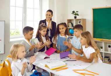Dost canlısı bir öğretmen ve sınıfta oynayan bir grup öğrenci. Gülümseyen öğretmen ve mutlu çocuklar okulda masanın etrafında beraber oyun oynuyorlar. Eğitim kavramı