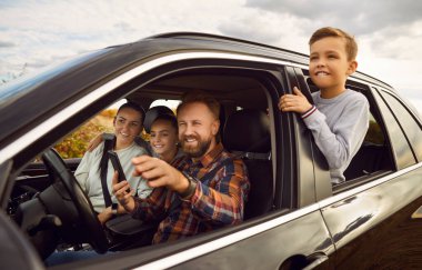 Dört çocuklu mutlu gülümseyen aile portresi. Arabada oturan ve araba süren çocuklar. Babam dijital harita uygulaması kullanıyor ve açık havayı gösteriyor ya da işaret ediyor. Yolculuk konsepti.