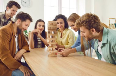 Bir grup mutlu genç kız ve erkek evde ahşap yapı taşlarıyla birlikte oynuyorlar. Masada oturup birlikte eğleniyorlar. Ev eğlencesi ve masa oyunları konsepti.