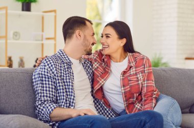 Evdeki oturma odasındaki kanepede oturan mutlu evli çiftin portresi. Kanepede birbirine bakan gülümseyen aile babası ve kadın. Ahenkli ilişkiler kavramı.