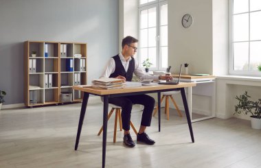 Ofiste çalışan, elinde dizüstü bilgisayar ve belgelerle masa başında oturan, profesyonelliği ve işe bağlılığı gösteren beyaz iş adamı ya da muhasebeci..