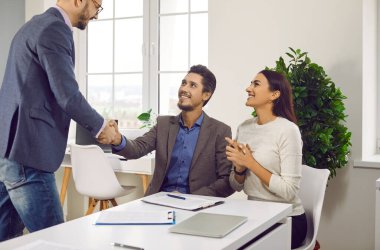 Erkek bir simsar ya da sigortacıyla tokalaşan mutlu bir çiftin portresi. Neşeli genç adam ve kadın ofiste oturan yatırım danışmanıyla iyi bir anlaşma yapıyorlar..