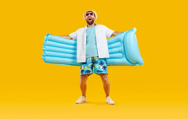 身穿白色夏衣 蓝色夏威夷假日短裤 太阳镜和太阳帽 头戴蓝色橡胶水垫 背景为黄色的快乐而快乐 兴奋的男人 假期的概念 — 图库照片