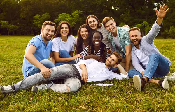 多様な大学生や友人たちが一緒に楽しく過ごしています 夏の公園の緑の草の上のグループの写真の肖像画をポーズする陽気な多角的な若者のチーム — ストック写真