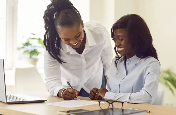 Woman loan broker, credit advisor or real estate agent meets with a client in her office. Two happy smiling young African American women sign a business contract agreement on the office desk
