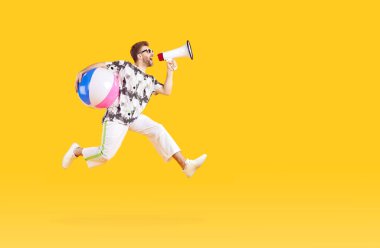 Komik, genç bir turistin portresi günlük giysiler içinde şişme plaj topu ile stüdyonun sarı arka planında ağza alınıp çığlık atan ve zıplayan. Tatil ve yaz tatili konsepti.