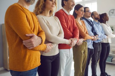 Farklı yaşlardan bir grup insan sıraya girip el ele tutuşuyorlar. Çok ırklı çok nesilli meslektaşlar ya da birlik ve destek gösteren topluluk üyeleri.