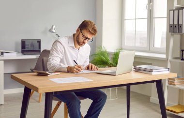 Ofiste ya da evde dizüstü bilgisayar üzerinde çalışan, notlar alan, hesaplamalar yapan, yeni projeler düşünen, şirketleri analiz eden kendine güvenen genç ve çekici bir iş adamı..