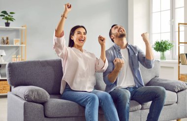 Mutlu genç aile çifti evdeki koltukta el kaldırıyor. Heyecanlı karı koca gol atmayı, favori takımlarının zaferini, piyangoyu kazanmayı ya da yeni eve taşınmayı kutluyor.