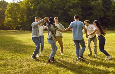 Bir grup insan parkın dışında el ele tutuşup çember oluşturarak oyun oynuyorlar. Güneşli bir yaz gününde gündelik kıyafetlerle oyun oynayıp dışarıda eğlenen mutlu öğrenciler..