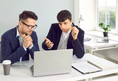 İş yerindeki işadamları. Takım elbiseli iki ciddi işveren dizüstü bilgisayarla masada oturuyor, konuşuyor ve tartışıyorlar, yeni projeler ya da girişimleri değerlendiriyorlar, şirketleri analiz ediyorlar..