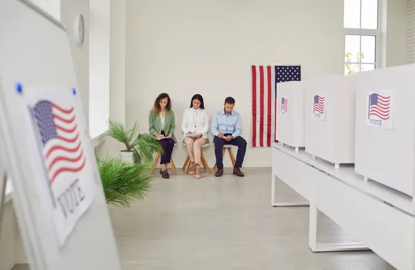 stock image Polling station with a row of white voting booths decorated with American flag at vote center. People american voters sitting at polling station. Democracy and election day concept.