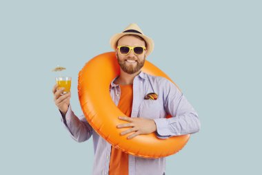 Şişme yüzüklü komik adam elinde bir bardak meyve suyu tutuyor ve tatile hazır gülümsüyor. Şişme yüzükle tatil hazırlığı deniz kenarı ya da havuz kenarında mutlu bir adam için tatil işareti.