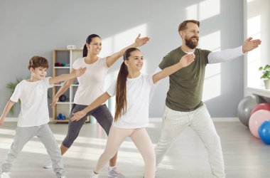 Genç, gülümseyen sporcu ebeveynler erkek ve kadın spor salonunda çocuklarla spor yapıyor. Mutlu bir aile birlikte antrenman yapıyor ve evde eğitim görüyor. Fitness ve sağlıklı yaşam tarzı konsepti.