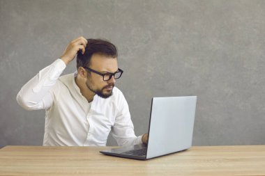 Portrait of confused man looking at computer screen. Puzzled employee, office worker, student or hipster feeling dumb and stupid trying to understand hard complicated stuff or fix PC software problem