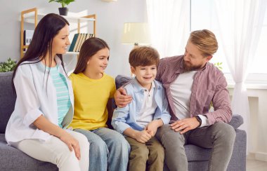 Gülümseyen dört çocuklu mutlu bir aile. İki kız ve erkek çocuk hafta sonunu birlikte geçirecekleri koltukta oturuyorlar. Neşeli ebeveynlerin çocuklu portresi. Aile zamanı ve eğlence konsepti.