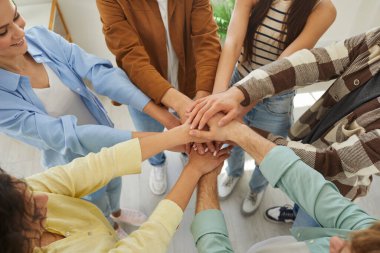 Mutlu gülümseyen genç insanların portresi ya da bir grup öğrencinin bir araya gelerek kollarını evde duran bir yığının içine koymaları. Arkadaşlık, birlik ve takım çalışması kavramı..