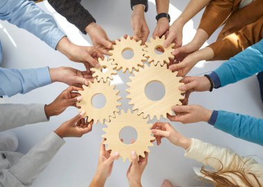 Business people or office workers hold wooden gears that symbolize well-coordinated teamwork. Top view close up of hands of multiracial men and women standing in circle. Concept business cooperation clipart