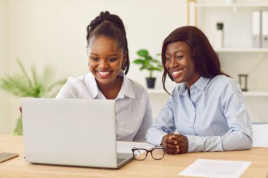 Genç Afro-Amerikalı kadınlar dizüstü bilgisayarla çalışıyor, ekrandan izliyorlar, gülümsüyorlar. Mutlu iş arkadaşları belge, sunum, e-posta, öğrenmek ve iletişim kurmak için birlikte çalışırlar.