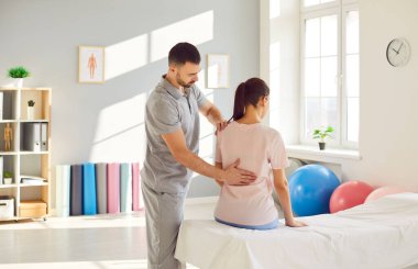 Erkek osteopat modern ofiste genç bir kadını muayene ediyor. Genç fizyoterapist rehabilitasyon kliniğinde bir kadını iyileştiriyor. Kayropraktik uzmanı omurga eğriliği ve sırt ağrısı olan hastaya yardım ediyor..