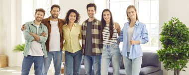 Memleketteki birkaç mutlu gencin toplu portresi. Pankart, altı genç erkek ve kadın arkadaşlarıyla birlikte oturma odasında durup kameraya bakıyor ve gülümsüyor.