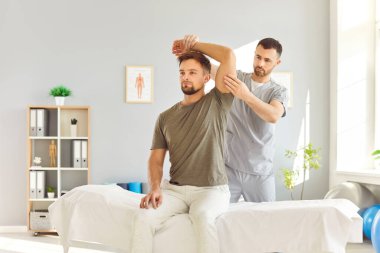 Kafkasyalı erkek fizyoterapist, bir hastaya sağlık hizmetleri rehabilitasyonu sırasında masaj ve kol germe terapisi sağlıyor. Fizik tedavi seanslarında tedavi uygulamaları.