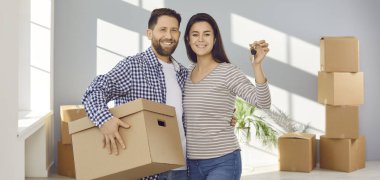 Anahtarı ve karton kutuları olan mutlu genç bir çift. Yeni apartman dairesinde durmuş kameraya bakıyor ve kutlama günü gülümsüyor. Taşınmak, gayrimenkul, ipotek konsepti. Pankart.