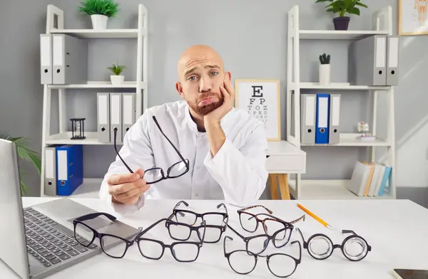 悲しい男眼科医がオフィスに座って眼鏡をかけている 彼の推測にもかかわらず 彼は重要な眼科ケアと眼科サービスを提供することに専念しています 眼科医療について — ストック写真