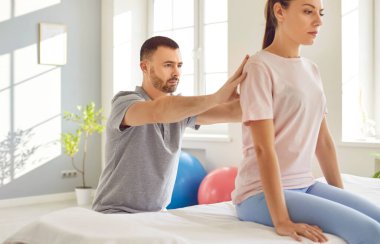 Genç doktor osteopat ya da fizyoterapist modern rehabilitasyon kliniğinde sırt ağrısını tedavi eden kadın hastaya yardım ediyor. Fizyoterapi ve fizik tedavi konsepti.