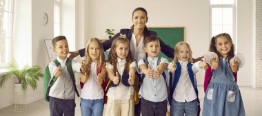 Pozitif ilkokul öğrencileri, kadın öğretmenle birlikte eğitici afiş veya çocuk için poz veriyorlar, ek eğitim önerileri, sınıfta duruyorlar